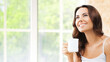 © vgstudio - Portrait of happy smiling brunette woman in white lingerie drinking coffee or tea, looking up, at home, near window and loft style wall.