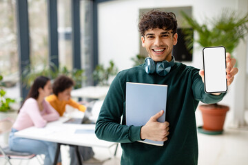 Positive european student guy showing smartphone with blank screen recommending educational app, coworking space