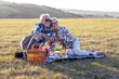 © pucko_ns - Charming senior couple enjoying a delightful picnic in the great outdoors. They are seen lounging comfortably on a checked blanket surrounded by a lush green landscape.