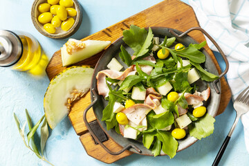 Wall Mural - Summer mediterranean salad with melon, bacon, olives, white cheese and arugula on blue stone background. Traditional Spanish and Italian appetizer.