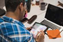 Latin Graphic Designer Working In His Office On An Illustration Tablet, He Wears A Blue Checkered Shirt And Glasses.