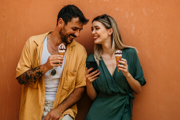 Wall Mural - A young tourist couple laughs as they share a large ice cream sundae, making the most of their day together in the city.