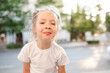 © morrowlight - Cute smiling kid girl 4-5 year old showing tongue having fun on city street over sunset background outdoor. Looking at camera. Summer season. Childhood.