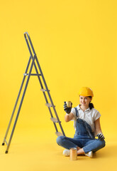 Canvas Print - Female decorator with cans of paint and stepladder on yellow background