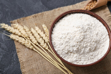 Bowl with wheat flour and spikelets on sackcloth, closeup