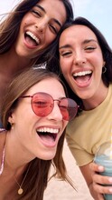 Vertical Of Three Excited Young Caucasian Friends In Summer Clothes Taking Selfie On Beach. Group Of Smiling Women Enjoying Vacation. Cheerful Beautiful Girls Of Generation Z Pose For Photo With Phone