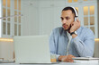 © New Africa - Young man with headphones working on laptop at desk in kitchen. Home office