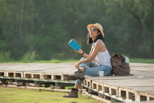 Asian Woman Traveler With Backpack Relaxing Outdoor With Sitting On Quayside Relax Read Book During Coffee Break On Background Summer Vacations And Lifestyle Hiking Concept.