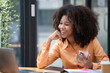 © Songsak C - Portrait of a beautiful confident businesswoman using a laptop computer holding a mobile phone sitting in a modern office. Smiling African American freelancer working online from home.