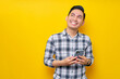 © Bangun Stock Photo - Smiling satisfied young Asian man wearing a white checkered shirt standing holding a mobile phone and looking at empty space isolated over yellow background. People Lifestyle Concept