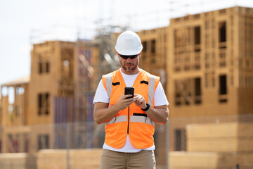 Wall Mural - Worker man on the building construction. Worker using phone, builder chatting on phone a break from work. Architect with mobile phone. Construction site worker outdoor portrait.