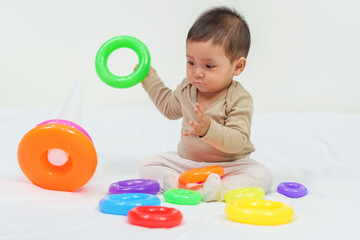 infant baby playing the pyramid toy with colored rings on bed