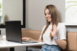 © Павел Костенко - A young freelance girl uses a laptop for a video call in a cafe. Smiles and waves, greets.