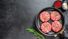 raw burgers - cutlets from organic beef meat with garlic and rosemary in a frying pan on black background, top view with copy space