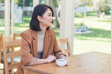 Asian Woman drink black coffee hand holding cup at green garden cafe. Young woman smile face love drink coffee. Beauty woman drinking black coffee in coffee shop holding freshness cup. Coffee lover