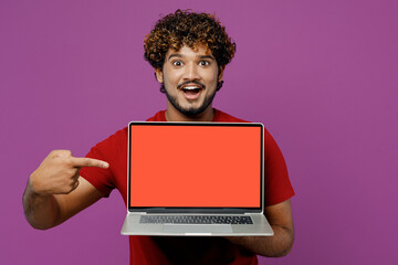 Wall Mural - Young shocked IT Indian man he wear red t-shirt casual clothes hold use work point on laptop pc computer with blank screen workspace area isolated on plain purple background studio. Lifestyle concept.