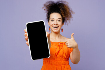 Young surprised latin woman wear orange blouse casual clothes hold in hand use mobile cell phone with blank screen workspace area show thumb up isolated on plain pastel light purple background studio.