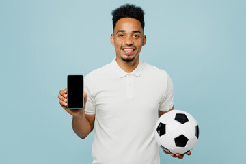 Young man fan wear basic t-shirt using blank screen mobile cell phone cheer up support football sport team hold in hand soccer ball watch tv live stream isolated on plain pastel blue color background.