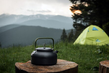 A Kettle On A Wooden Table In A Mountain Campsite. A Tent And Mountains Are In The Background.