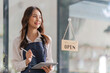 © Natee Meepian - Asian woman barista holding tablet for checking order from customer on blurred coffee cafe shop background , SME business concept