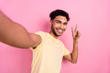 Wall Mural - Portrait of optimistic pleasant man afro hair earrings stubble recording video for blog showing v-sign isolated on pink color background