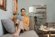 © Natee Meepian - Beautiful attractive young Asian woman sitting on gray sofa and using digital tablet at living room in the morning