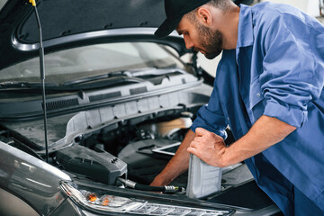 Grey colored oil can in hands. Auto mechanic working in garage. Repair service