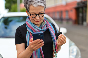 Poster - A senior woman with a smartphone in her hands and car keys uses a rental app.