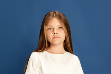 half-length portrait of charming little girl looking at camera over blue background. kids emotions, 