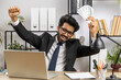 © Andrii Iemelianenko - Indian businessman holding fan of cash money dollar banknotes celebrate, dance, success career, lottery jackpot game winner, big income, wealth at home office workplace desk. Remote distant working