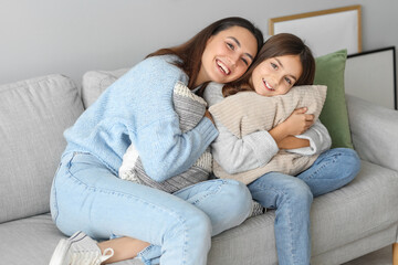 Wall Mural - Little girl and her mother in warm sweaters with pillows sitting on sofa at home