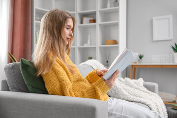 Wall Mural - Young woman reading book on sofa at home