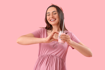 Sticker - Young pregnant woman with glass of smoothie making heart on pink background