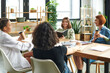 © LIGHTFIELD STUDIOS - happy young woman reading from notebook near multiethnic female friends drinking coffee from paper cups in interest club, knowledge-sharing and socializing concept