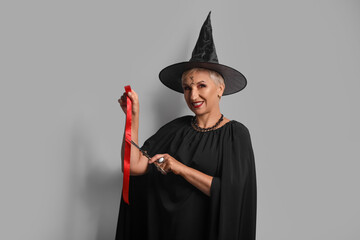 Mature witch cutting ribbon on grey background