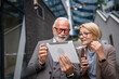 © Miljan Živković - senior man dressed in a suit and a mature blonde woman as business partners husband and wife friends or colleagues talk With digital tablet in hand browse internet look data exchange ideas copy space