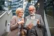 © Miljan Živković - senior man dressed in a suit and a mature blonde woman as business partners husband and wife friends or colleagues talk With digital tablet in hand browse internet look data exchange ideas copy space