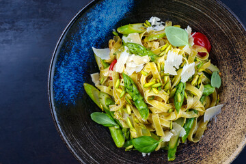 Traditionelle italienische Tagliatelle mit grünem Spargel, Tomaten und gehackten Pistazien serviert als Draufsicht auf einem Nordic Design Teller