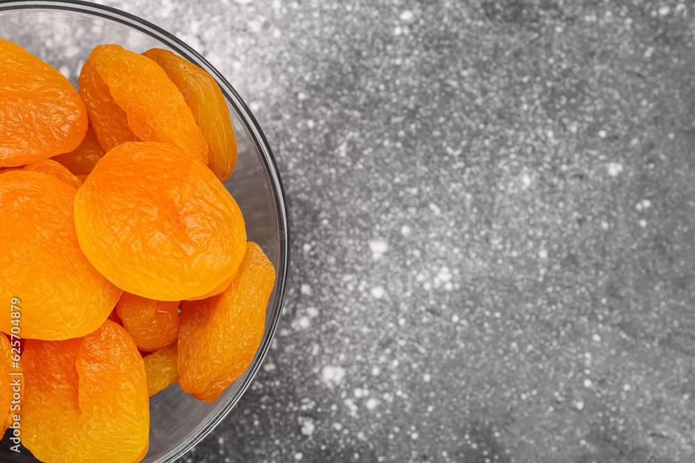 Glass bowl with tasty dried apricots on grey background