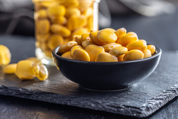 Sticker - Lupini beans in brine. Pickled lupin in bowl on black table.