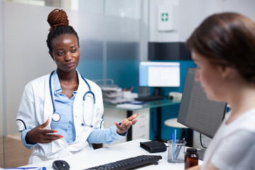 Wall Mural - African american doctor talking with patient, offering check-up consultation in medical office. Woman receiving professional examination from consulting general practitioner