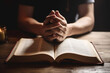 © ADDICTIVE STOCK - Generative AI illustration of crop anonymous person in dark cloth praying with clasped hand over sacral book on wooden table in dark room