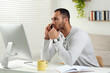 © New Africa - Young man talking on smartphone while working with computer at desk in room. Home office
