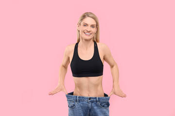 Sticker - Slim woman wearing big jeans on pink background. Weight loss