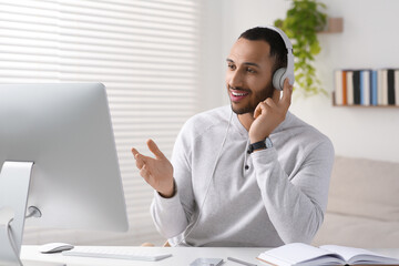 Canvas Print - Young man with headphones working on computer at desk in room. Home office