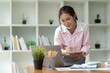 © Phimwilai - Office worker or businesswoman, attractive Asian woman in eyeglasses researching Analyze information about the business plan. take notes in a book Notebook while using a laptop computer at her desk.
