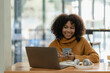 © ArLawKa - Focused young african college student working on laptop in living room and learning online using laptop computer. Smiling girl watching webinar or distance education class