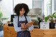 © ArLawKa - Beautiful african american female cashier or barista writes purchase details and checks availability small business owner A coffee shop wearing an apron stands in front of the counter.