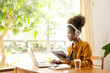 © ArLawKa - Focused young african college student working on laptop in living room and learning online using laptop computer. Smiling girl watching webinar or distance education class