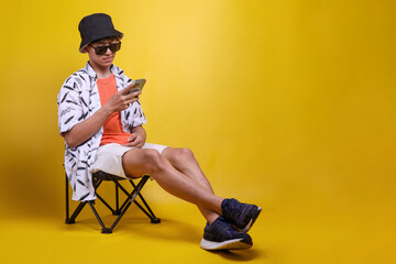 Full length profile side photo of guy traveler sit relax on deckchair while using smartphone. Holiday, leisure and people concept